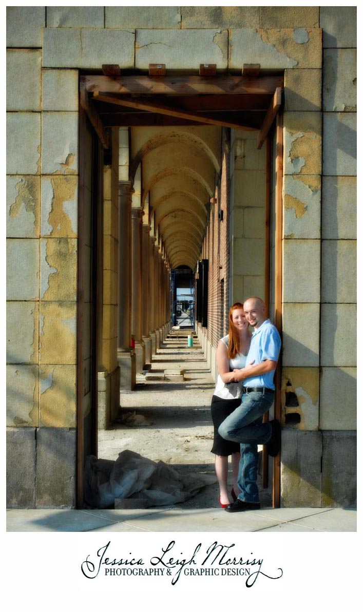 Couple embraces under a series of repeating stone archways, framed by textured walls and dramatic lines in golden afternoon light.