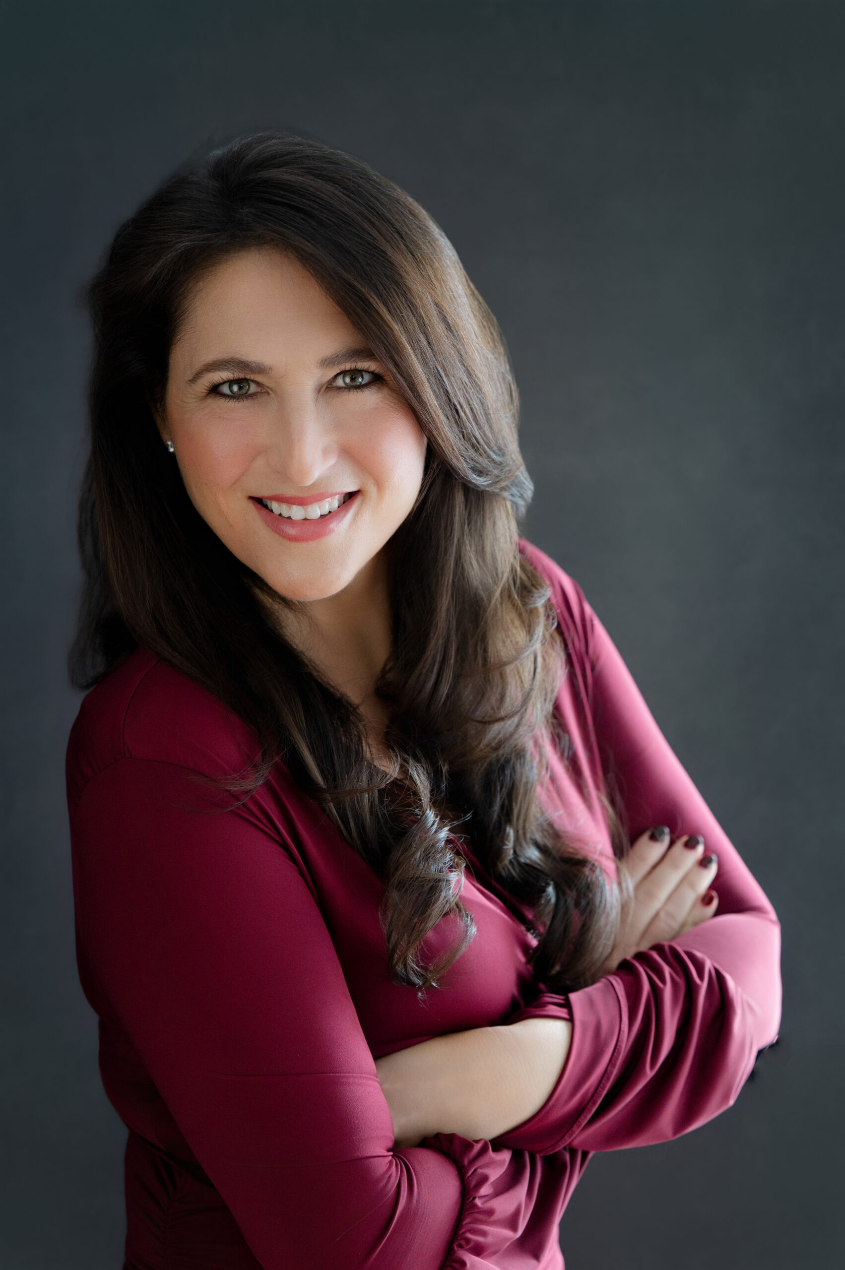 Professional studio headshot of a smiling woman with arms crossed against a dark background